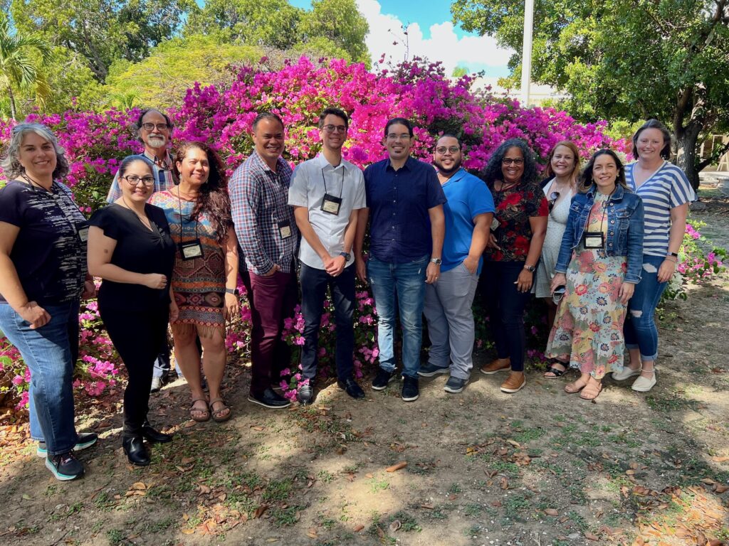 Whole group pose of participants standing in front of vibrant pink flower bushes
